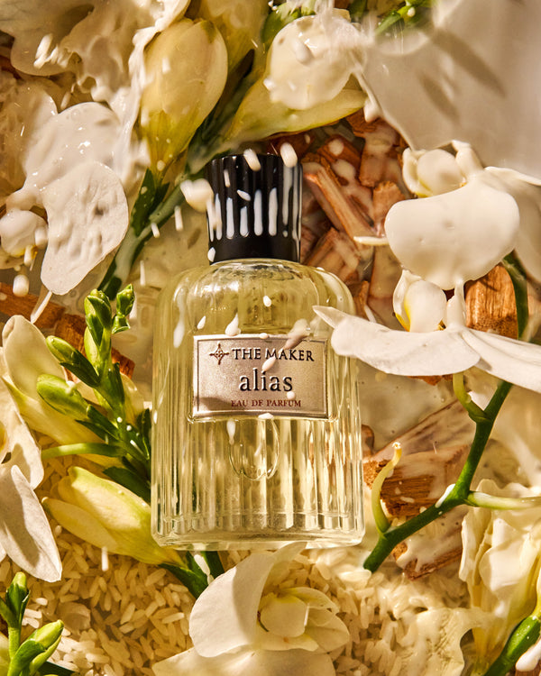 Perfume bottle labeled 'The Maker alias' surrounded by white flowers
