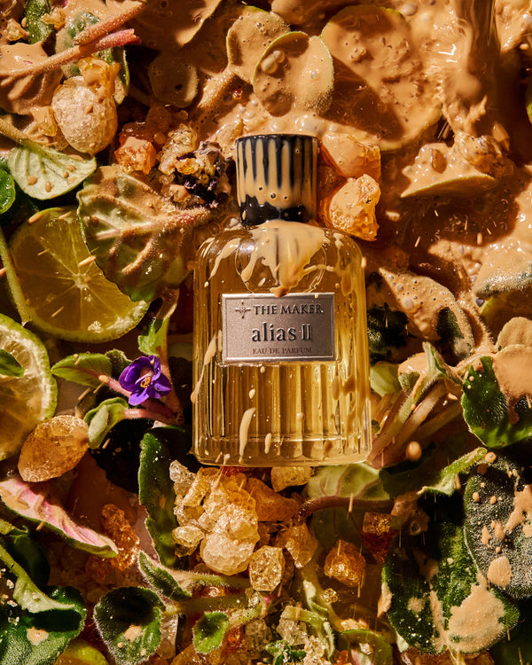 Perfume bottle labeled 'alias II' surrounded by natural elements like leaves and stones.