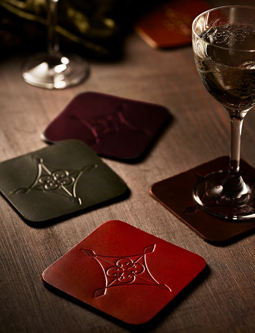 Leather coasters with embossed designs on a wooden surface with glasses of wine.